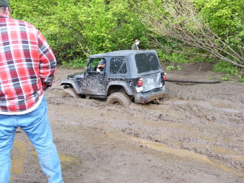 1980 Ford Bronco - A black Jeep Wrangler is stuck in deep mud, with a person in a plaid shirt watching.