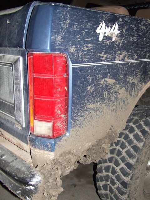 1986 Ford Bronco - Muddy rear quarter panel and taillight of a blue SUV, showing '4x4' decal. Supermotors.net logo is present.