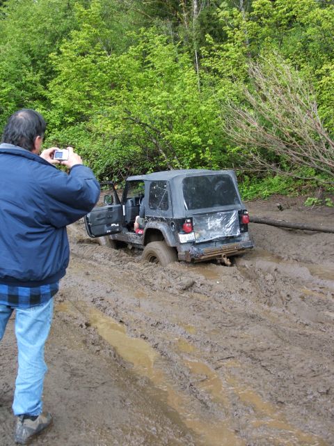 1980 Ford Bronco - A Jeep is stuck in thick mud on a wooded trail, with a person taking a photo of the scene.