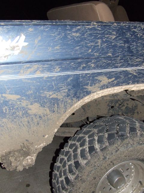 1986 Ford Bronco - Mud-covered blue SUV side view, with a glimpse of the interior seat and a Supermotors watermark.