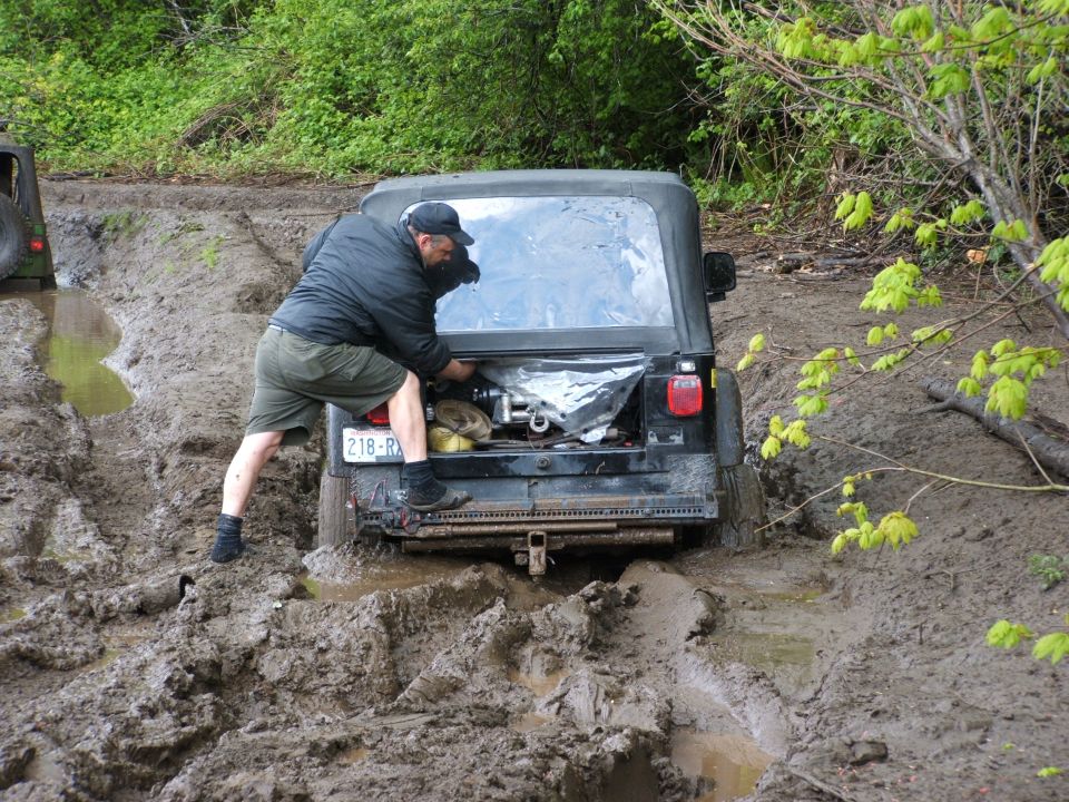 Black Jeep Wrangler stuck in mud, driver working on rear