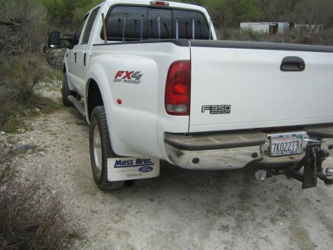 1990 Ford Bronco - Rear three-quarter view of a white Ford F-350 Super Duty crew-cab dually pickup with FX4 off-road badging, parked on a dirt lot.