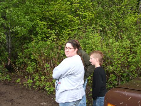 1980 Ford Bronco - A brown vehicle fender is visible in the foreground with people standing behind it in a wooded area.