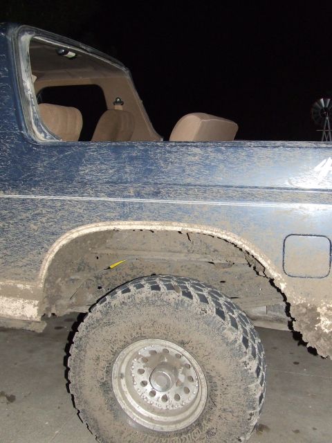 1986 Ford Bronco - 1986 Ford Bronco rear side view with mud covering the body and tire.