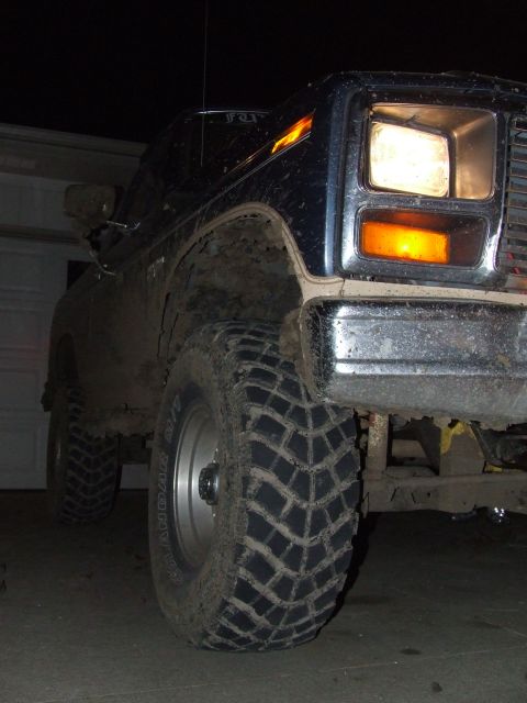 1986 Ford Bronco - Front corner view of a dark blue 1986 Ford Bronco, equipped with large off-road tires, parked in a garage at night.