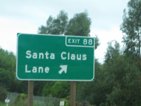 1990 Ford Bronco - Green roadside guide sign reading Santa Claus Lane, Exit 88, with an up-right arrow, framed by trees.