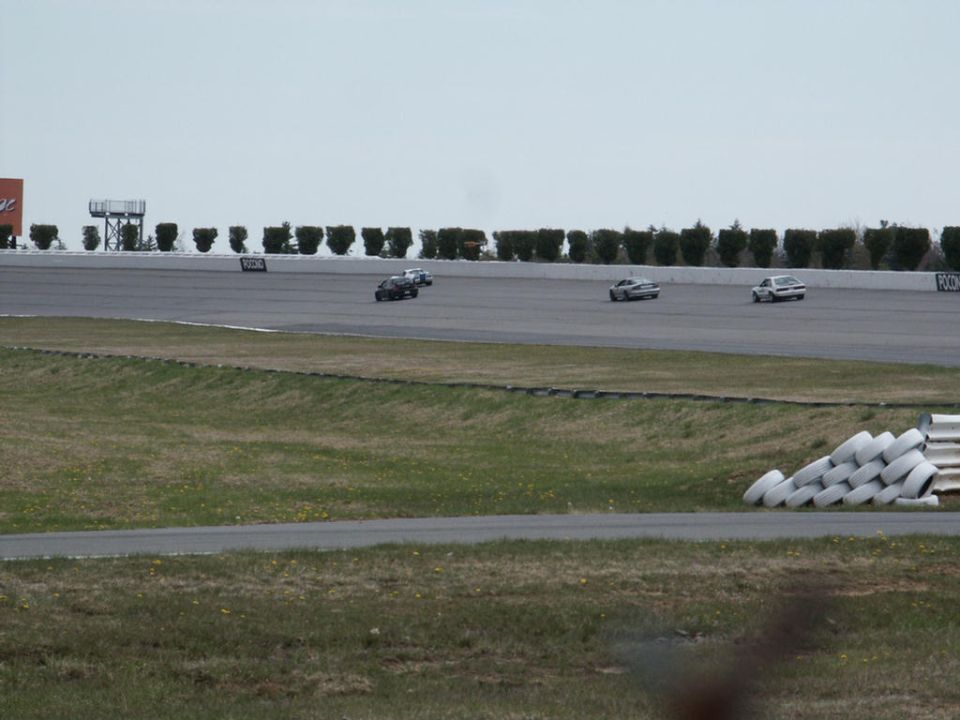 Cars racing on a track with tire barriers and trees in the background