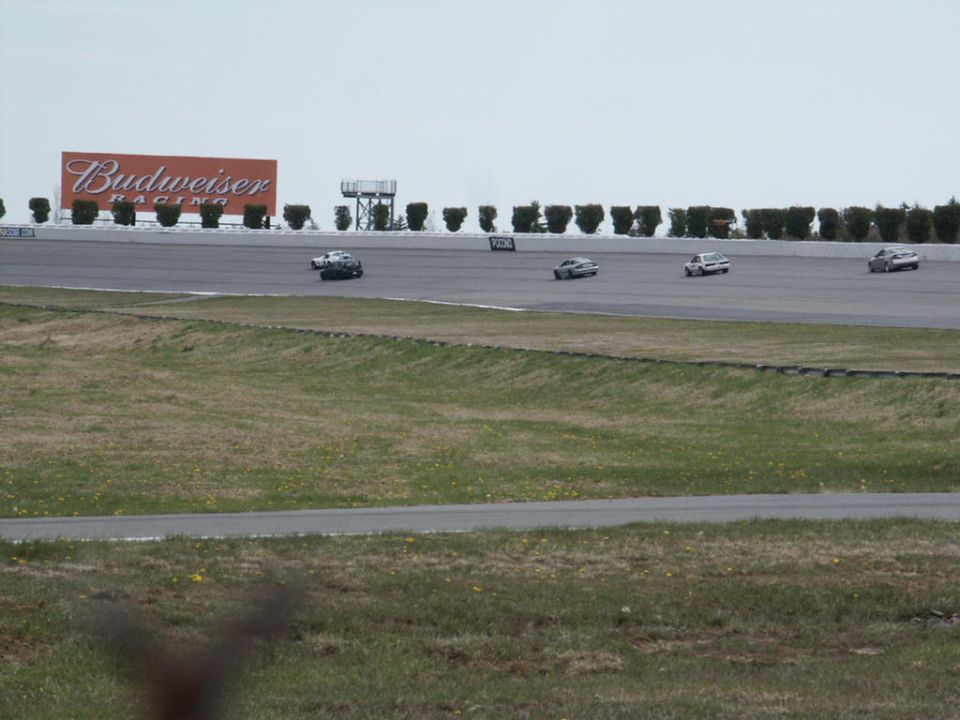 Several cars race on a track with a Budweiser sign in the background