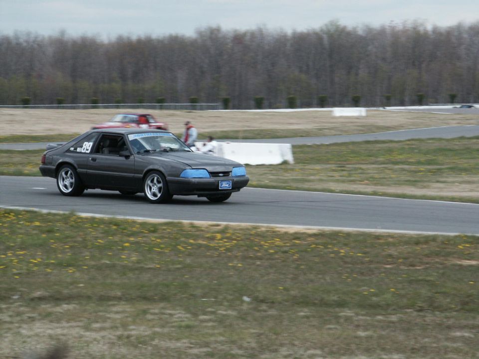 Dark gray coupe with blue headlights and number 89 on the door, driving on a race track