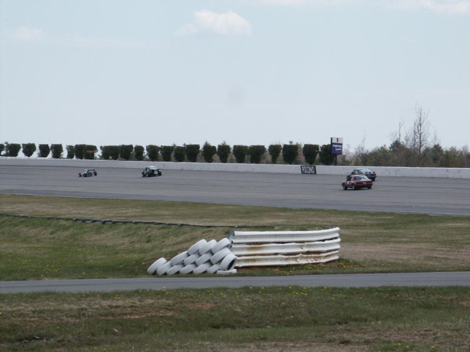Several race cars on a track with tire barriers and trees in the background