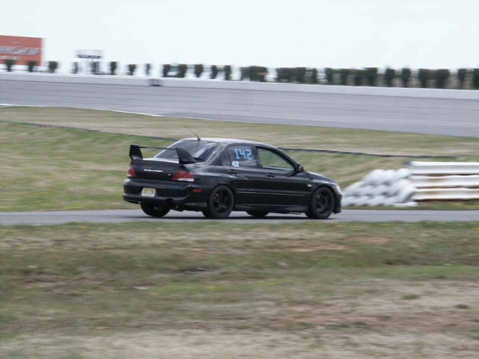 Black Mitsubishi Lancer Evolution VIII with racing numbers 142 on the door, seen from a 3/4 front angle on a race track