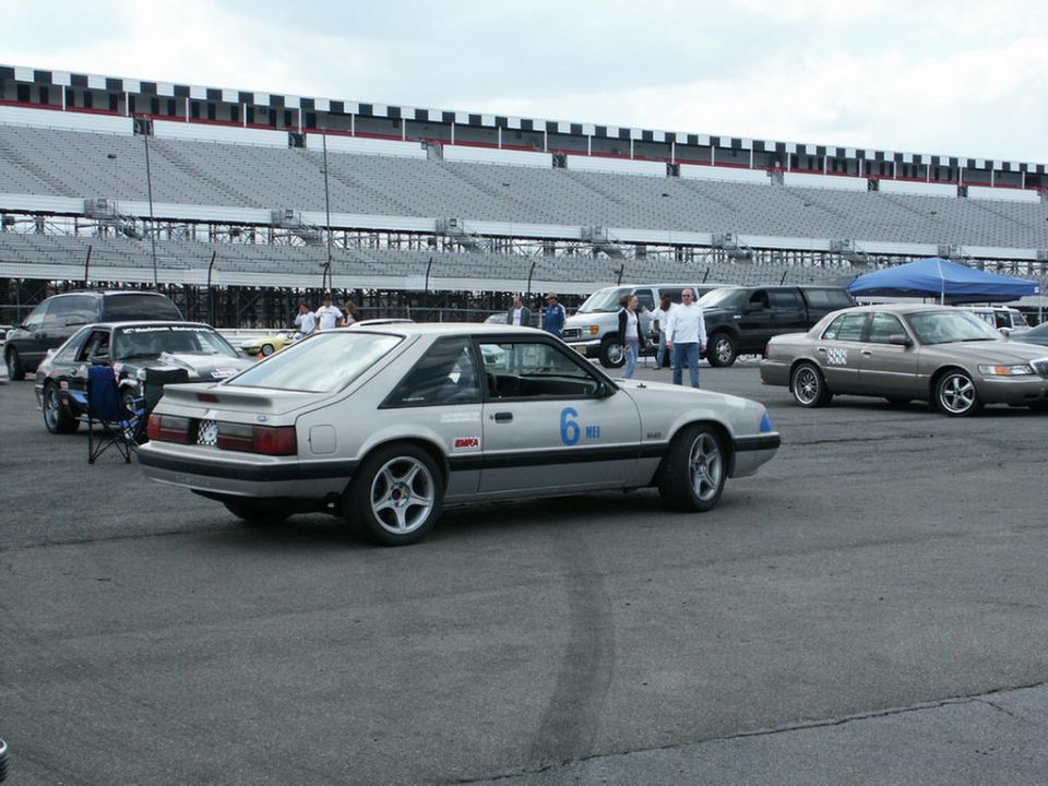 Silver coupe with racing number 6 and 'EMRA' decal on the side, parked at a racetrack