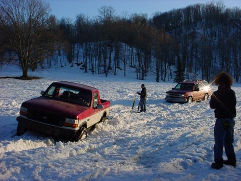 2000 Chevrolet Tahoe - A red and white pickup truck is stuck in deep snow, with another SUV visible in the background.
