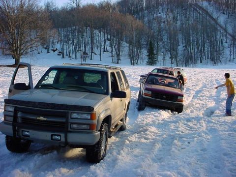 2000 Chevrolet Tahoe - Several vehicles are stuck in the snow on a hill with trees in the background.
