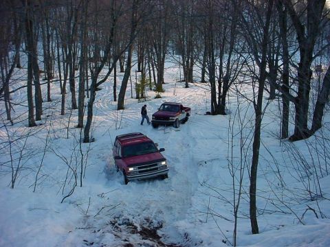 2000 Chevrolet Tahoe - Two vehicles navigate a snow-covered path through a wooded area.