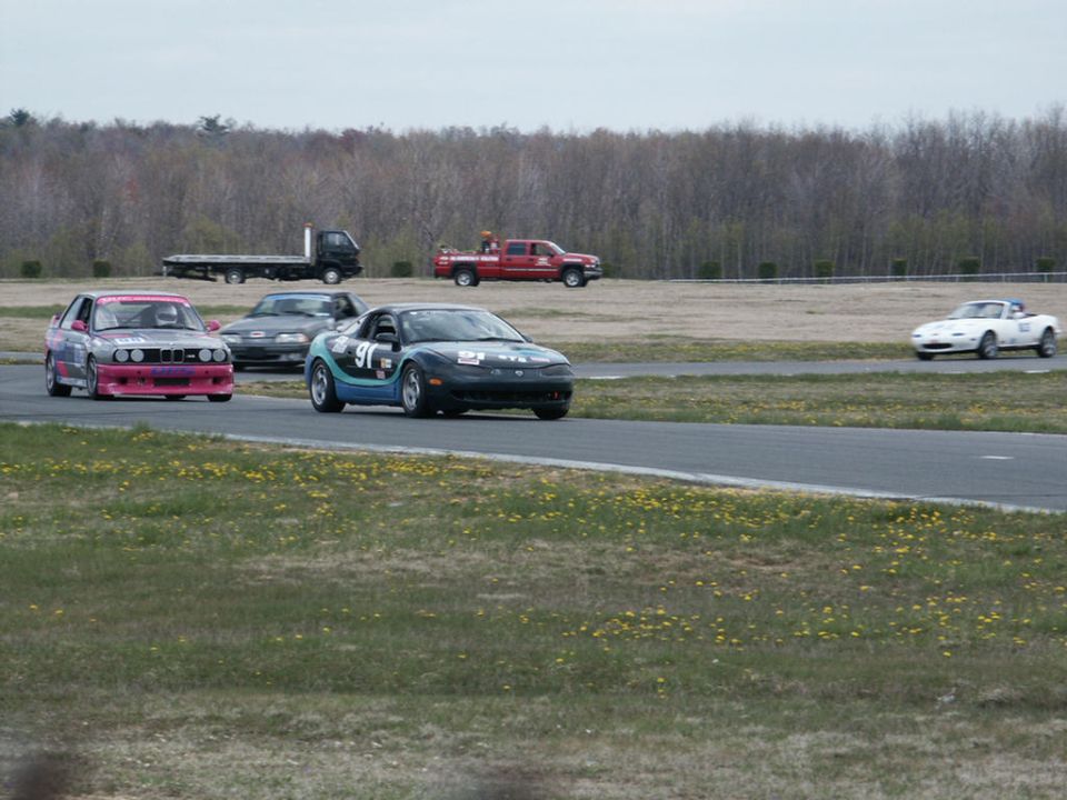 Several race cars on a track, including a black car with blue and green decals and number 91