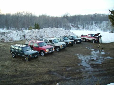 2000 Chevrolet Tahoe - Several SUVs and a pickup truck are parked in a muddy lot with snow piles and bare trees visible.