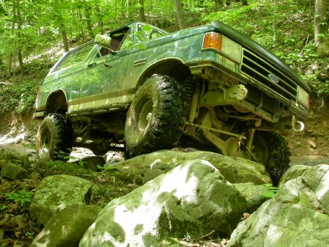 1990 Ford Bronco - This 1990 Ford Bronco navigates a challenging rocky path through a dense forest.