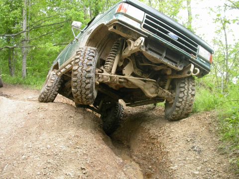 1990 Ford Bronco - Green Ford Bronco navigates a challenging off-road trail, its lifted suspension and aggressive tires.