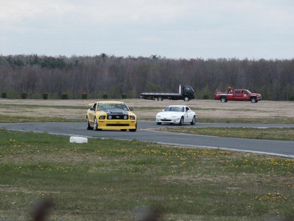 Yellow Ford Mustang with black hood stripes and white Mazda Miata on a race track