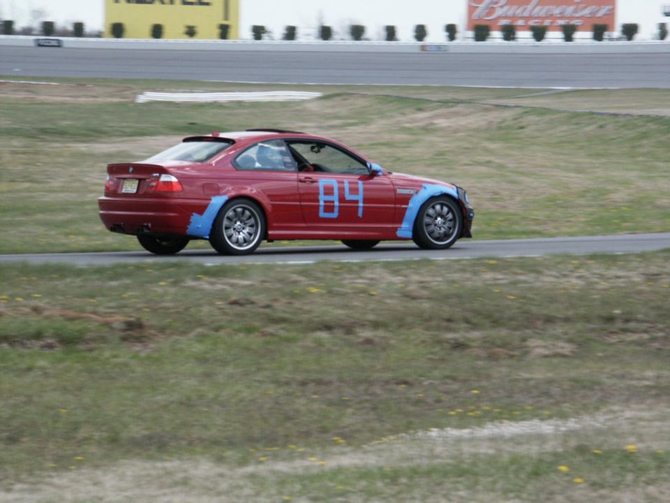Red coupe with blue fender flares and number 84 on the door, driving on a track