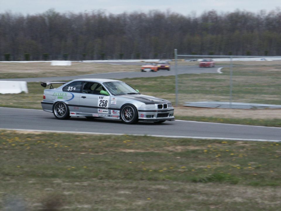 Silver BMW M3 E36 with racing decals and number 258 on a track, other cars in background