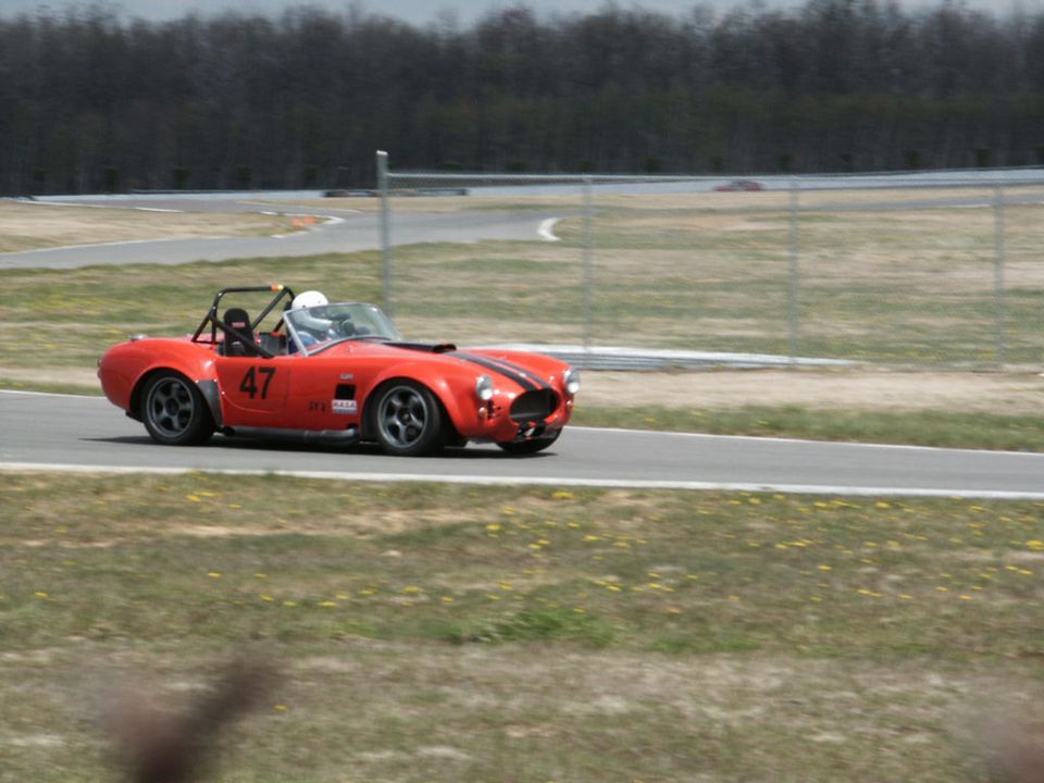 Red convertible sports car with black racing stripes and number 47 on the door, on a race track