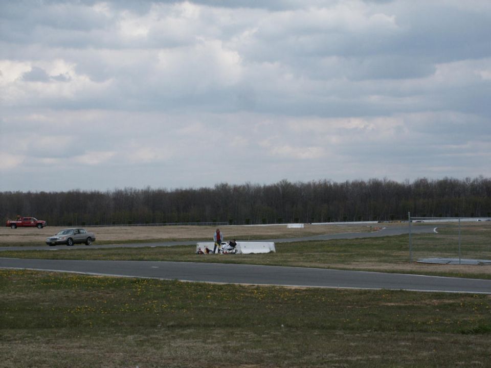 Silver sedan on race track with red truck in distance