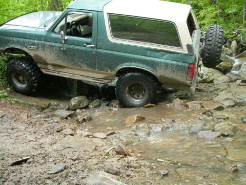 1990 Ford Bronco - This Ford Bronco is navigating a challenging off-road trail with water and rocks.