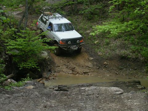 1990 Ford Bronco - White 1990 Ford Bronco tackles a challenging muddy obstacle on an off-road trail.