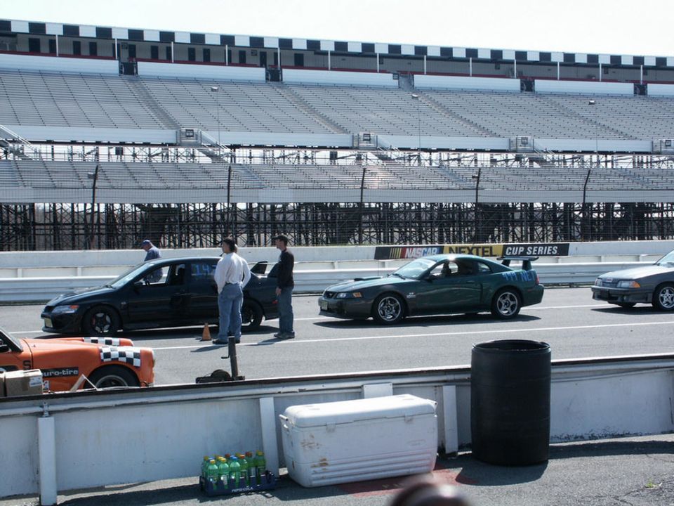 Green Ford Mustang Cobra with a spoiler on a racetrack, next to a black sedan and a gray car