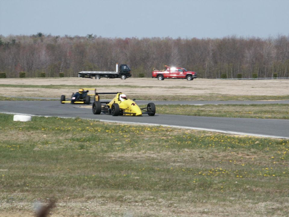 Yellow formula race car on track with another car behind it