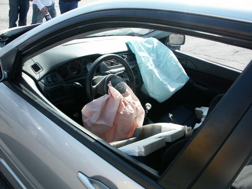 Silver car interior, driver's side, with deployed airbags, damaged dashboard, and steering wheel