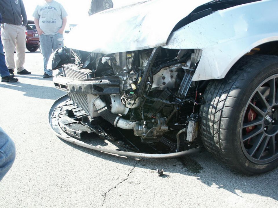 Front end of a damaged car showing exposed engine components and a bent bumper