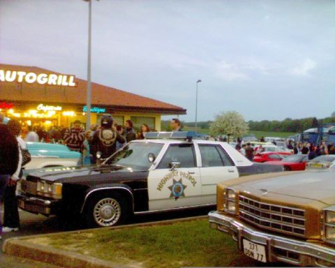 1991 Ford Crown Victoria - A police car is parked in front of a building with people gathered around.