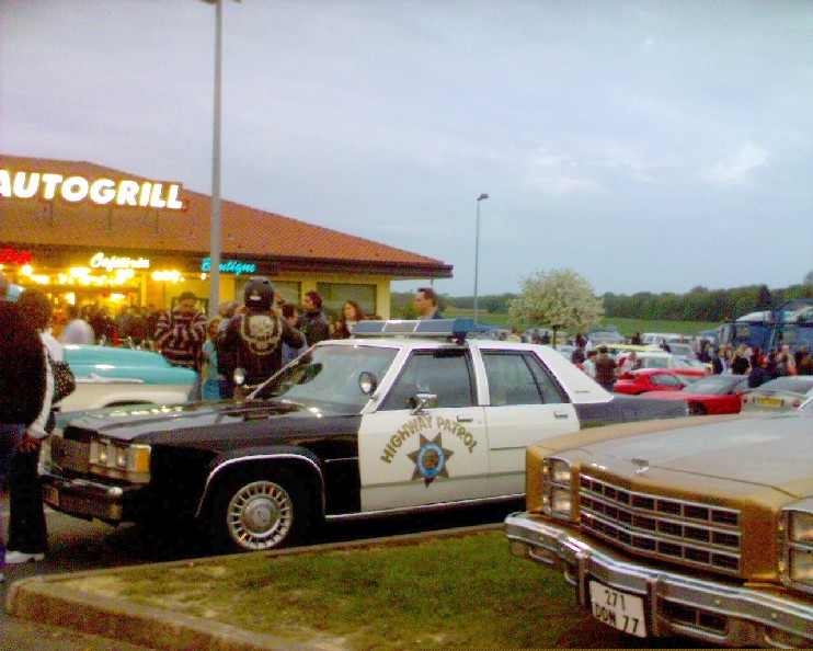 Black-and-white Highway Patrol Crown Victoria at an evening car meet outside an Autogrill