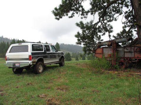 1994 Ford C-350 (Centurion Conversions) - A two-tone 1994 Ford Bronco Centurion Conversion SUV is parked in a field, with an old piece of farm machinery to its right.