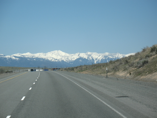Open highway leading toward snow-capped mountains under a clear blue sky.