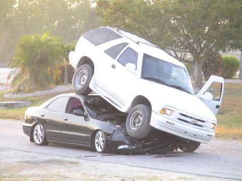 1993 Ford C-350 (Centurion Conversions) - Two vehicles involved in a severe accident on a road with trees in the background.