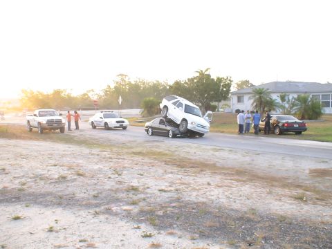 1993 Ford C-350 (Centurion Conversions) - An accident scene with a white SUV precariously balanced on top of a dark sedan.