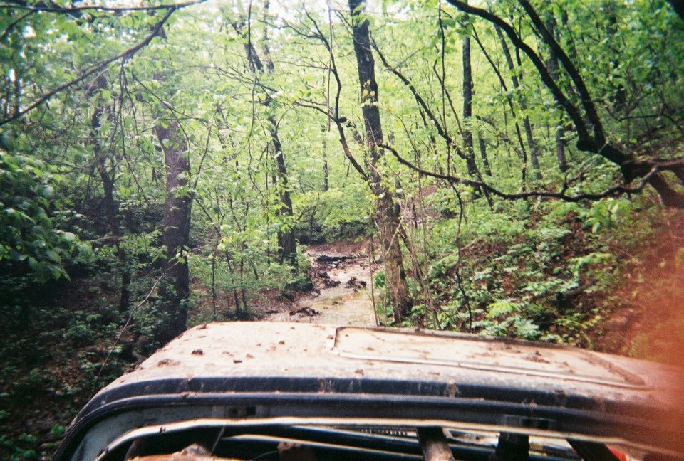 View from inside a vehicle looking out at a muddy, wooded trail