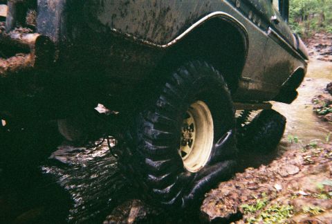 1978 Ford Bronco - A 1978 Ford Bronco navigates a muddy off-road course, its large tires kicking up water and dirt.