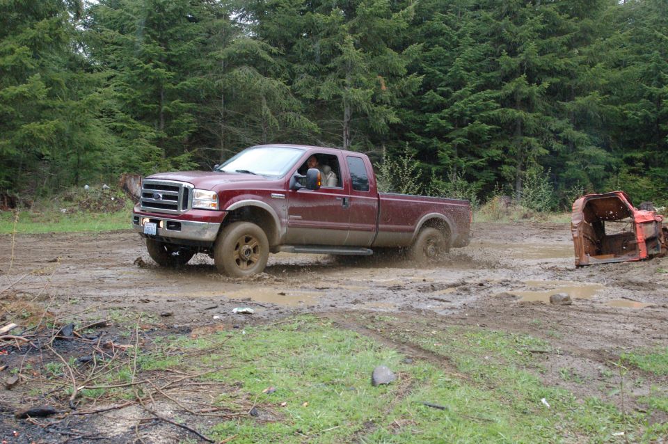 Maroon Ford F-250 extended-cab pickup spinning through mud in a forest clearing.
