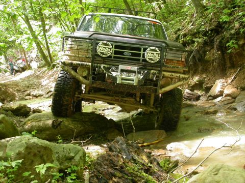 1990 Ford Bronco - A modified Ford Bronco navigates a challenging off-road course with a winch and brush guard.