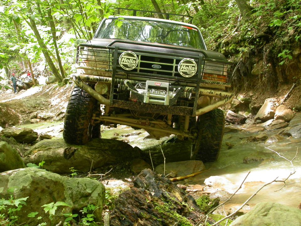 Black Ford Bronco off-roading through a rocky stream, front view