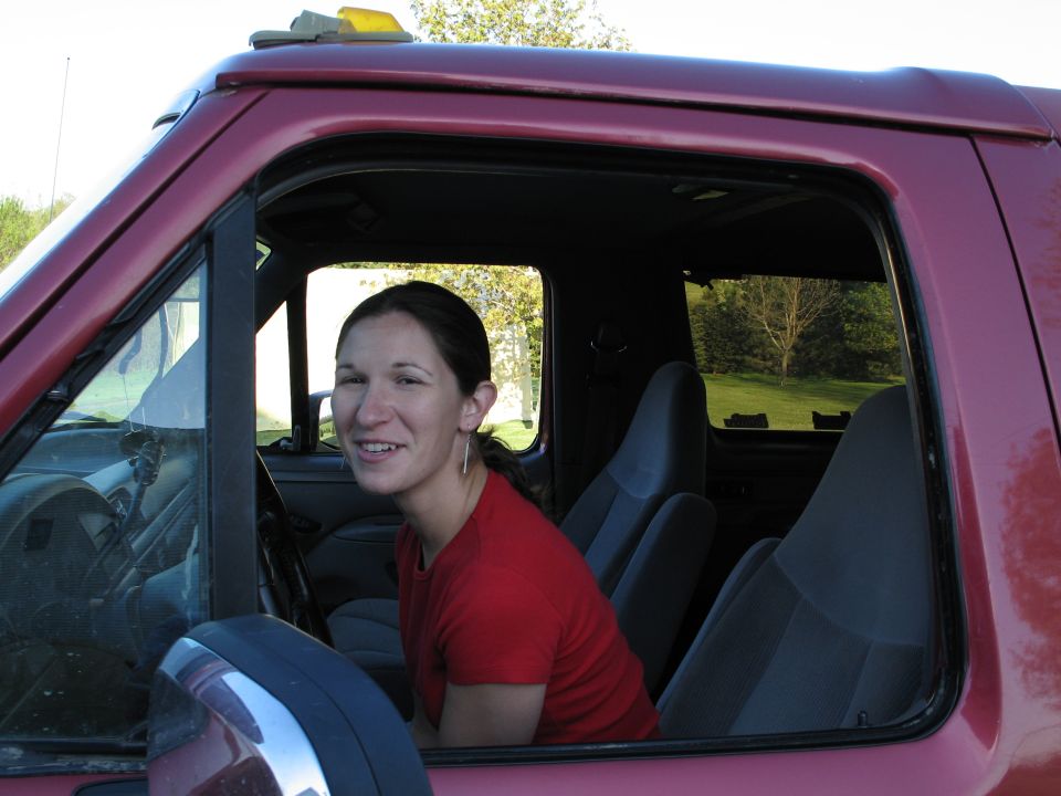 Woman in a red shirt sitting in the driver's seat of a dark red truck with gray cloth seats