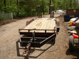 1995 Ford Bronco - An open car hauler trailer with a wooden deck and metal frame is parked outdoors on a dirt road.
