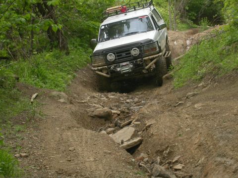 1990 Ford Bronco - White Ford Bronco tackles a challenging off-road path with a rocky stream bed.