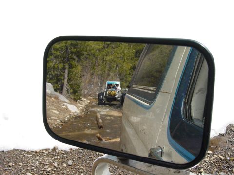 1986 Ford Bronco - A buggy navigates a watery dirt road, seen reflected in the side mirror of another vehicle.
