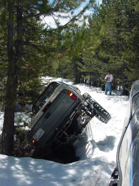 1986 Ford Bronco - An off-road vehicle is stuck in a snowy ditch, with another vehicle partially visible to the right.